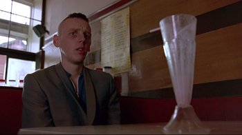 Movie still from “Trainspotting” (1996), directed by Danny Boyle – A man sitting at a table in front of a glass of milk; Close Up shot, Low angle