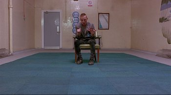 Movie still from “Trainspotting” (1996), directed by Danny Boyle – A man sitting on top of a chair in a room; Wide shot, High angle