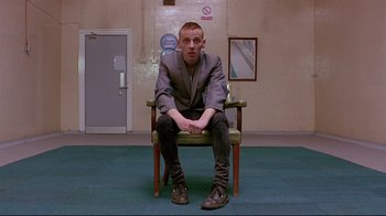 Movie still from “Trainspotting” (1996), directed by Danny Boyle – A man sitting on a chair in a room; Medium shot, Low angle