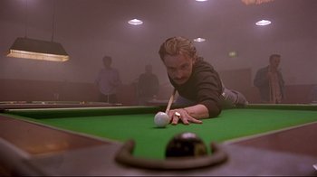 Movie still from “Trainspotting” (1996), directed by Danny Boyle – A man is playing a game of pool while others watch; Medium shot, Low angle