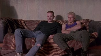 Movie still from “Trainspotting” (1996), directed by Danny Boyle – A couple of men sitting on top of a brown couch; Medium shot, Low angle