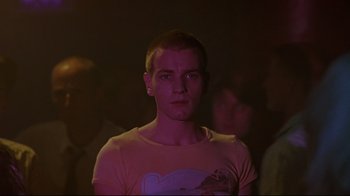 Movie still from “Trainspotting” (1996), directed by Danny Boyle – A young man is standing in a dark room; Close Up shot, Low angle