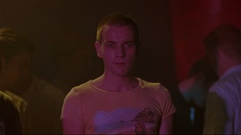 Movie still from “Trainspotting” (1996), directed by Danny Boyle – A young man in a yellow shirt in a dark room; Medium shot, Low angle