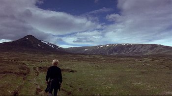Movie still from “Trainspotting” (1996), directed by Danny Boyle – A person standing in a field with mountains in the background; Extreme Wide shot, High angle