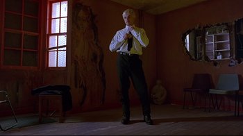 Movie still from “Trainspotting” (1996), directed by Danny Boyle – A man standing in a dimly - lit room tying his tie; Wide shot, Low angle