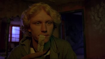 Movie still from “Trainspotting” (1996), directed by Danny Boyle – A man with blonde hair is eating a piece of food; Close Up shot, Low angle