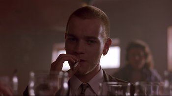 Movie still from “Trainspotting” (1996), directed by Danny Boyle – A man in a suit smoking a cigarette in front of a glass of water; Close Up shot, Low angle