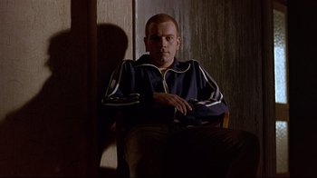 Movie still from “Trainspotting” (1996), directed by Danny Boyle – A man sitting in a chair in a dark room; Medium shot, Low angle