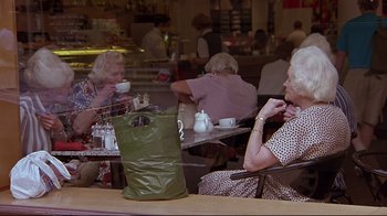 Two older women sitting at a table with a green bag
