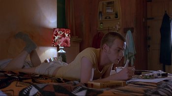 Movie still from “Trainspotting” (1996), directed by Danny Boyle – A man laying on the floor writing on a book; Medium shot, Low angle