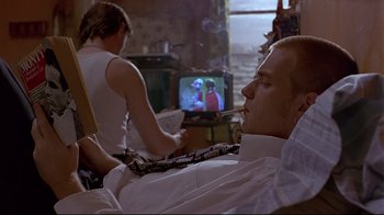 Movie still from “Trainspotting” (1996), directed by Danny Boyle – A man sitting in front of a tv while smoking a cigarette; Medium shot, Over the shoulder angle