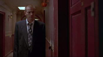 Movie still from “Trainspotting” (1996), directed by Danny Boyle – A man in a suit and tie standing in front of an open door; Medium shot, Low angle
