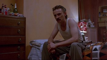 Movie still from “Trainspotting” (1996), directed by Danny Boyle – A man sitting on a bed in a room; Medium shot, Low angle
