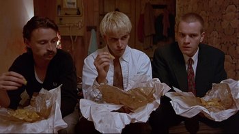 Movie still from “Trainspotting” (1996), directed by Danny Boyle – A group of men sitting around a table eating food; Medium shot, Low angle