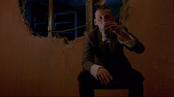 Movie still from “Trainspotting” (1996), directed by Danny Boyle – A man in a suit and tie drinking from a cup; Medium shot, Low angle