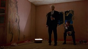 Movie still from “Trainspotting” (1996), directed by Danny Boyle – A man in a suit and tie standing in a room; Wide shot, Low angle