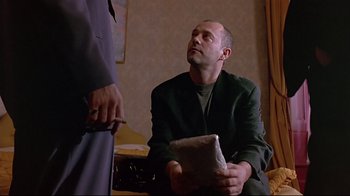 Movie still from “Trainspotting” (1996), directed by Danny Boyle – A man sitting on the ground holding a book; Medium shot, Low angle