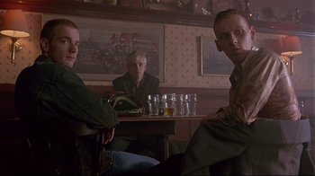 Movie still from “Trainspotting” (1996), directed by Danny Boyle – A group of people sitting at a table with drinks; Medium shot, Low angle