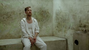 Movie still from “True Detective” (2014), created by Issa López – A man sitting on a bench with his hands in his pockets; Medium shot, Over the shoulder angle