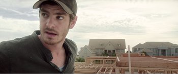 Movie still from “99 Homes” (2014), directed by Ramin Bahrani – A person wearing a hat near a house; Close Up shot, Over the shoulder angle
