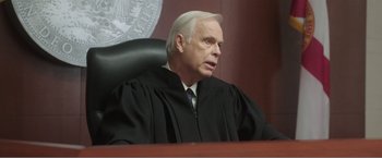 Movie still from “99 Homes” (2014), directed by Ramin Bahrani – An older man wearing a black robe and a black tie; Close Up shot, Low angle