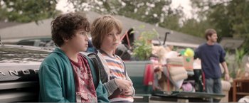 Movie still from “99 Homes” (2014), directed by Ramin Bahrani – Two young boys standing next to each other in a parking lot; Medium shot, Over the shoulder angle