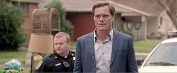 Movie still from “99 Homes” (2014), directed by Ramin Bahrani – A man standing next to another man in a police uniform; Close Up shot, Over the shoulder angle