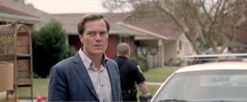 Movie still from “99 Homes” (2014), directed by Ramin Bahrani – A man standing in front of a police car; Close Up shot, Over the shoulder angle