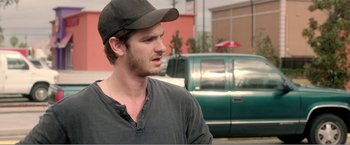 Movie still from “99 Homes” (2014), directed by Ramin Bahrani – A man wearing a baseball cap standing in front of a car; Close Up shot, Over the shoulder angle
