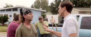 Movie still from “99 Homes” (2014), directed by Ramin Bahrani – A man talking to another man in front of other men; Medium shot, Over the shoulder angle