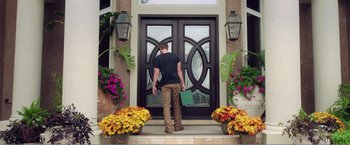 Movie still from “99 Homes” (2014), directed by Ramin Bahrani – A man standing in front of an open door of a house; Wide shot, Low angle