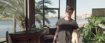 Movie still from “99 Homes” (2014), directed by Ramin Bahrani – A man standing in front of a window with a view of the ocean; Medium shot, Over the shoulder angle