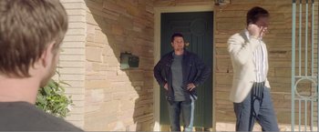 Movie still from “99 Homes” (2014), directed by Ramin Bahrani – A man standing in front of a door wearing a jacket; Wide shot, Low angle