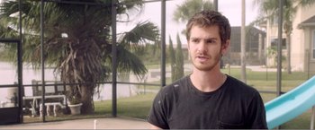 Movie still from “99 Homes” (2014), directed by Ramin Bahrani – A man standing in front of a window with trees in the background; Close Up shot, Over the shoulder angle