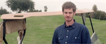 Movie still from “99 Homes” (2014), directed by Ramin Bahrani – A man in a blue shirt is standing in the grass; Close Up shot, Over the shoulder angle