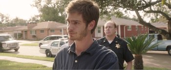 Movie still from “99 Homes” (2014), directed by Ramin Bahrani – A man in a blue shirt is in front of two other men; Close Up shot, Over the shoulder angle