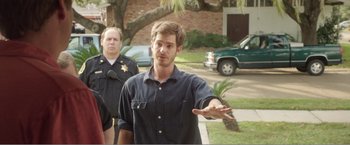 Movie still from “99 Homes” (2014), directed by Ramin Bahrani – A man in a black shirt is holding his hand out to a cop; Medium shot, Over the shoulder angle