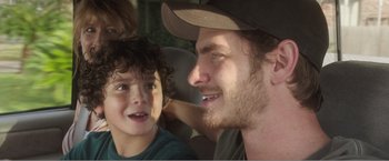 Movie still from “99 Homes” (2014), directed by Ramin Bahrani – A man and a boy in a car smiling for the camera; Close Up shot, Over the shoulder angle