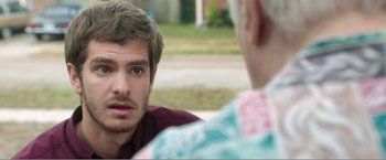 Movie still from “99 Homes” (2014), directed by Ramin Bahrani – A man sitting next to another man on the street; Close Up shot, Over the shoulder angle