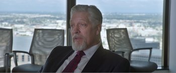 Movie still from “99 Homes” (2014), directed by Ramin Bahrani – An older man in a suit and tie in front of a window; Close Up shot, Over the shoulder angle