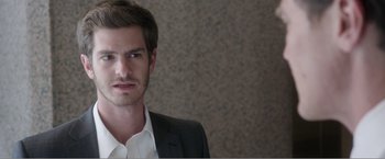 Movie still from “99 Homes” (2014), directed by Ramin Bahrani – A man wearing a suit and tie standing in front of a wall; Close Up shot, Over the shoulder angle
