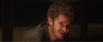 Movie still from “99 Homes” (2014), directed by Ramin Bahrani – A person with a beard smiling; Close Up shot, Over the shoulder angle