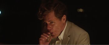 Movie still from “99 Homes” (2014), directed by Ramin Bahrani – A person holding a cigar; Close Up shot, Low angle