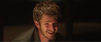 Movie still from “99 Homes” (2014), directed by Ramin Bahrani – A person with a beard smiling; Close Up shot, Over the shoulder angle