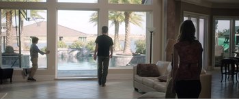 Movie still from “99 Homes” (2014), directed by Ramin Bahrani – A man standing in front of a large window; Wide shot, Over the shoulder angle