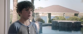 Movie still from “99 Homes” (2014), directed by Ramin Bahrani – A young boy standing in front of a swimming pool; Close Up shot, Over the shoulder angle