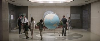 Movie still from “99 Homes” (2014), directed by Ramin Bahrani – A group of people standing in front of a large globe; Wide shot, High angle