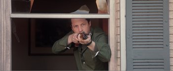 Movie still from “99 Homes” (2014), directed by Ramin Bahrani – A man holding a gun while standing next to a window; Medium shot, Over the shoulder angle