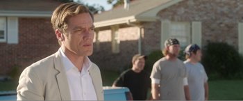 Movie still from “99 Homes” (2014), directed by Ramin Bahrani – A man standing in front of two other men outside; Close Up shot, Over the shoulder angle