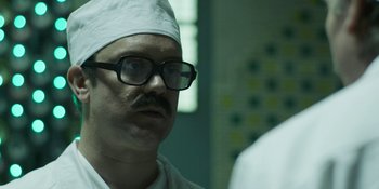 Movie still from “Chernobyl” (2019), directed by Johan Renck – A man wearing a white hat and glasses in a room; Close Up shot, Over the shoulder angle